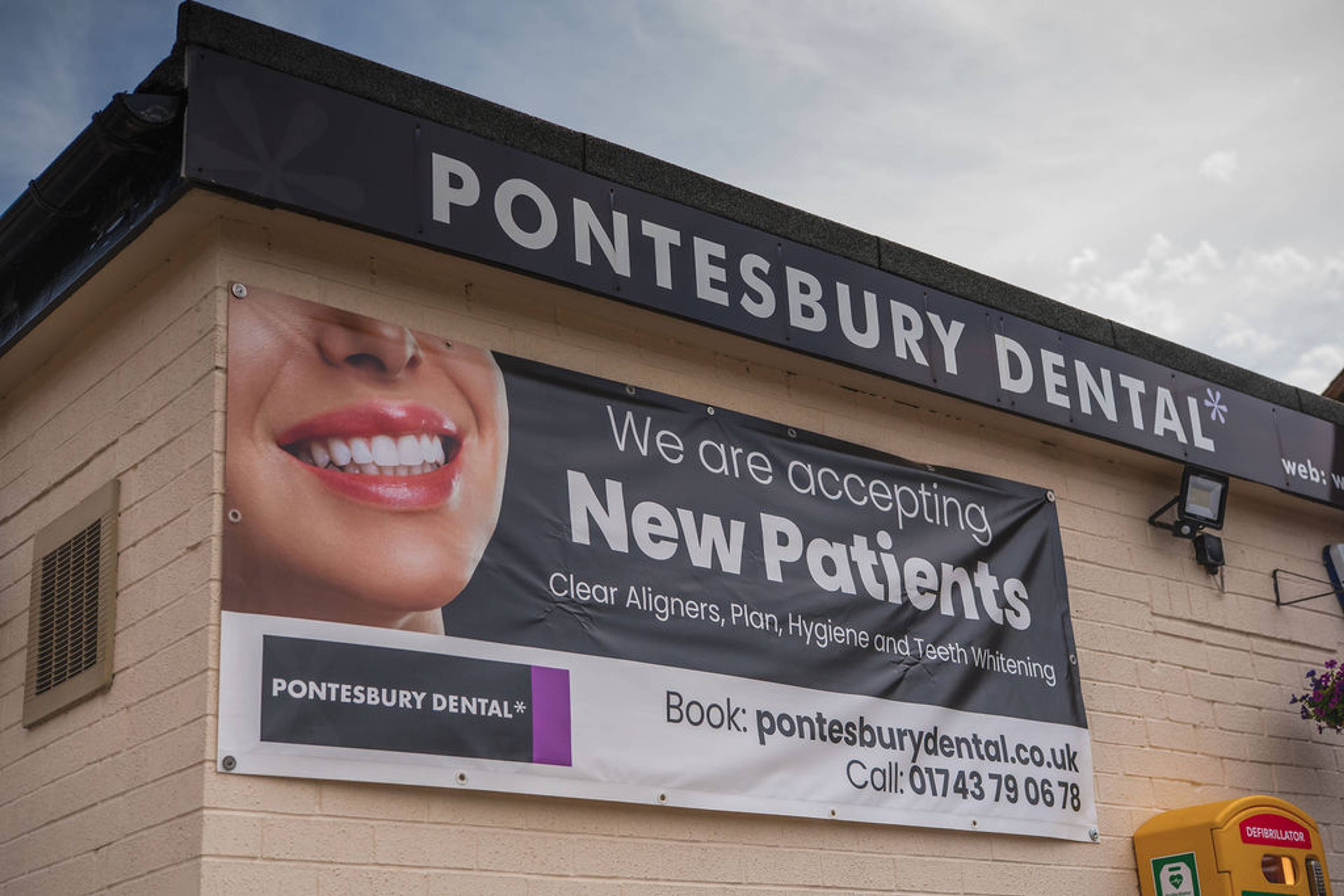 Exterior sign and new patient banner displayed on the front of the Pontesbury Dental clinic building.