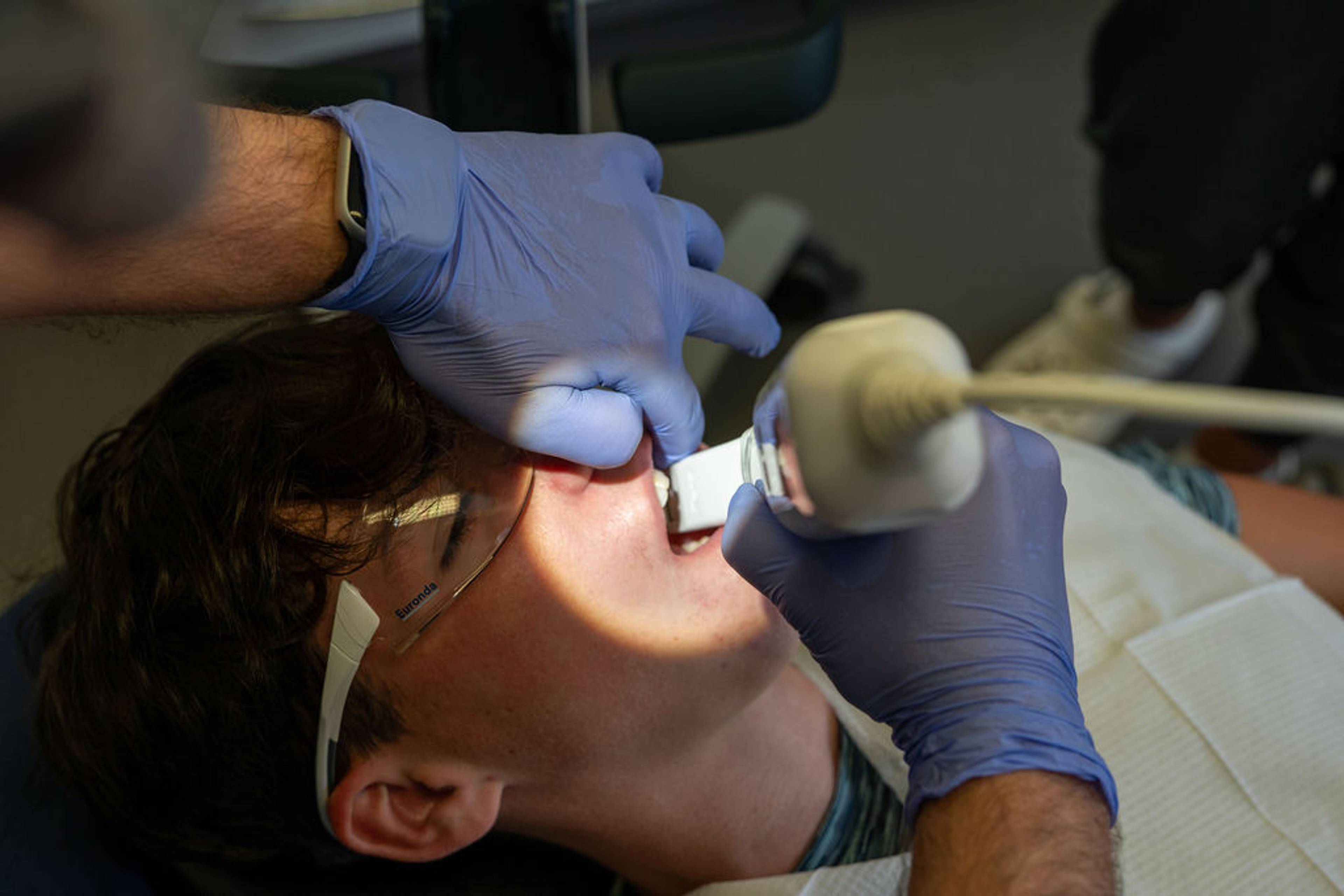 Patient wearing protective glasses undergoing a dental examination while a clinician uses an intraoral camera to capture images inside the mouth.
