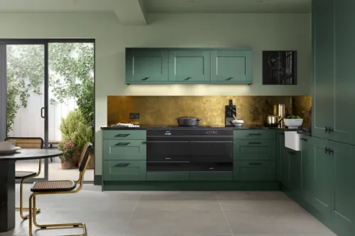 Green and gold kitchen interior with shaker cabinetry and black solid worksurfaces