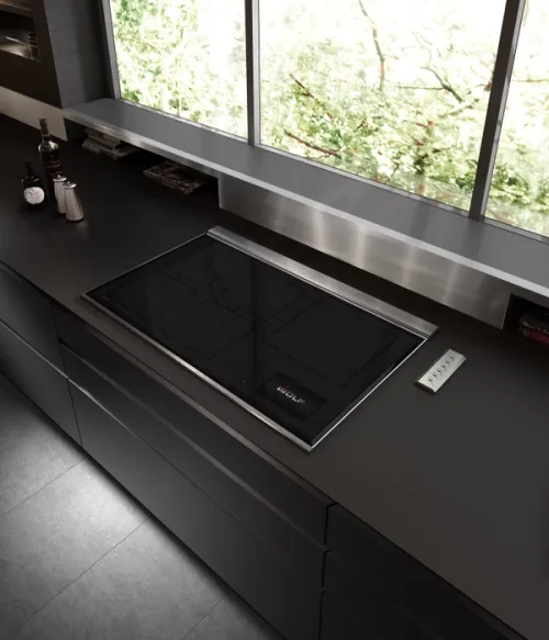 Black glass and stainless steel induction hob in a dark kitchen scene.