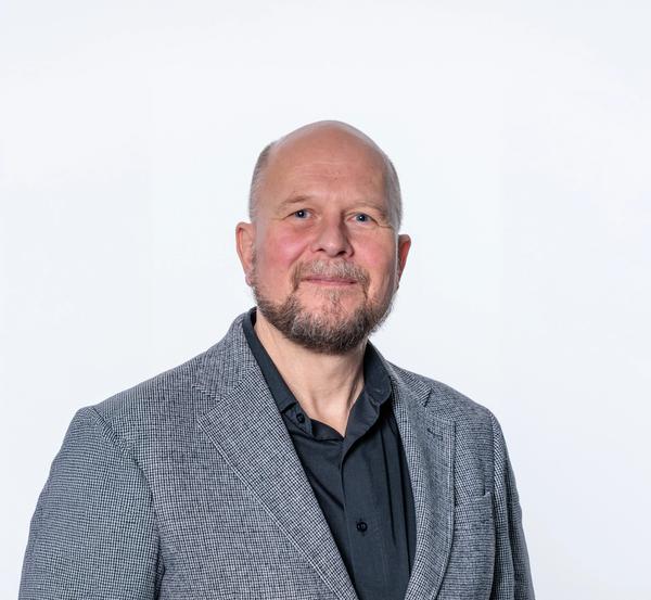 Headshot of a smiling bald man with a beard, wearing a grey blazer.