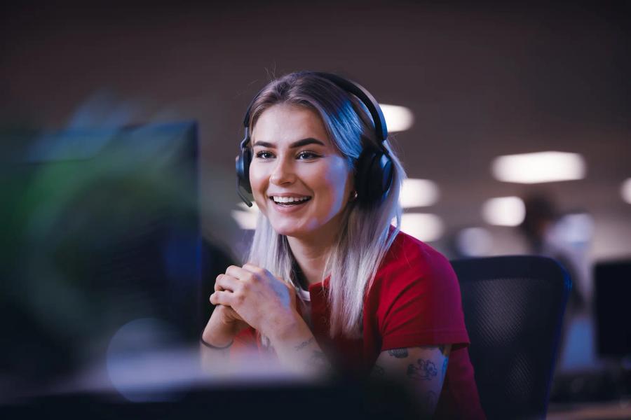 A woman wearing headphones is smiling while sitting in front of a computer.