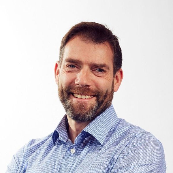Headshot of a smiling man with a beard wearing a blue patterned shirt.