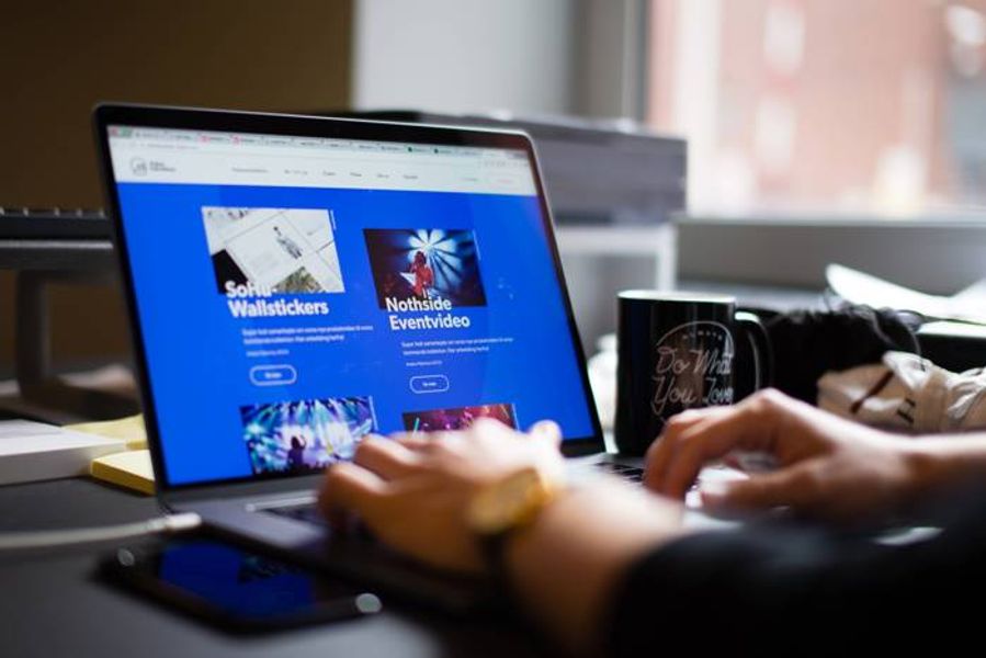 Hands typing on a laptop displaying a blue website, with a "Do What You Love" mug and smartphone nearby.