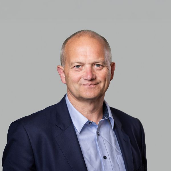 Headshot of a smiling man with short gray hair, wearing a blue shirt and navy blazer.