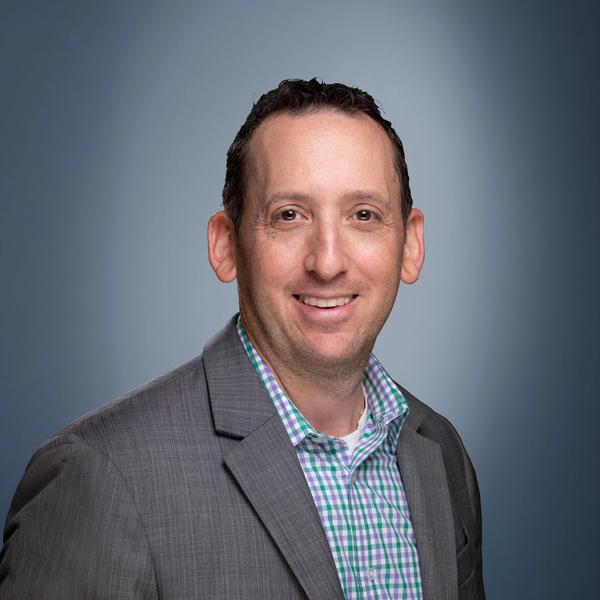 Headshot of a smiling man with a beard wearing a blue patterned shirt.