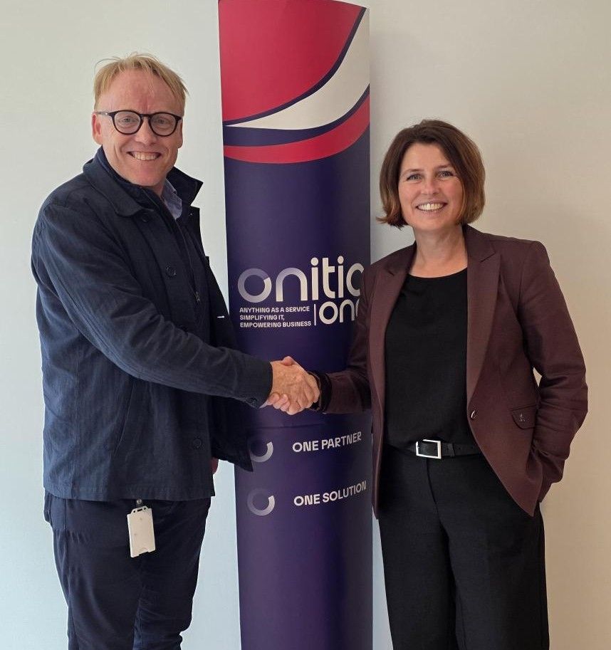A man and woman shake hands and smile, standing in front of an Onitica banner.