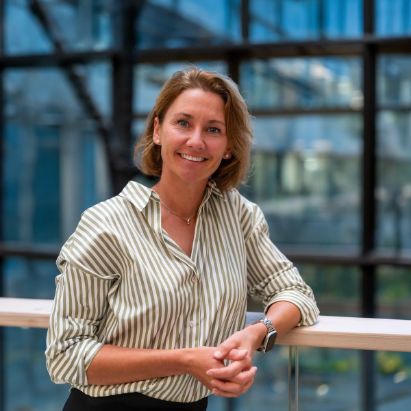 Smiling woman with short blonde hair wearing a striped shirt, leaning on a railing.