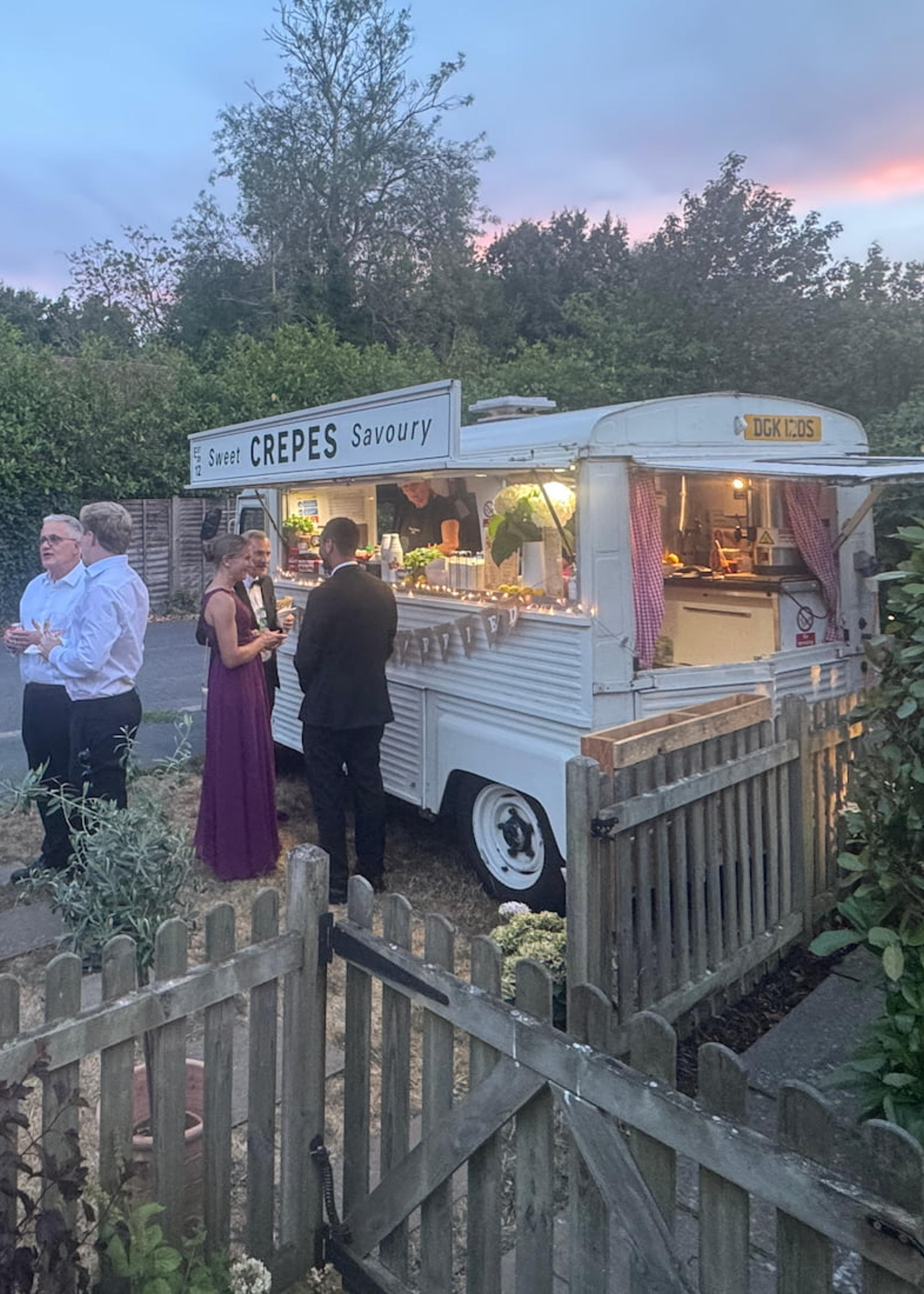 Wedding guests gathered around the crepe van at dusk