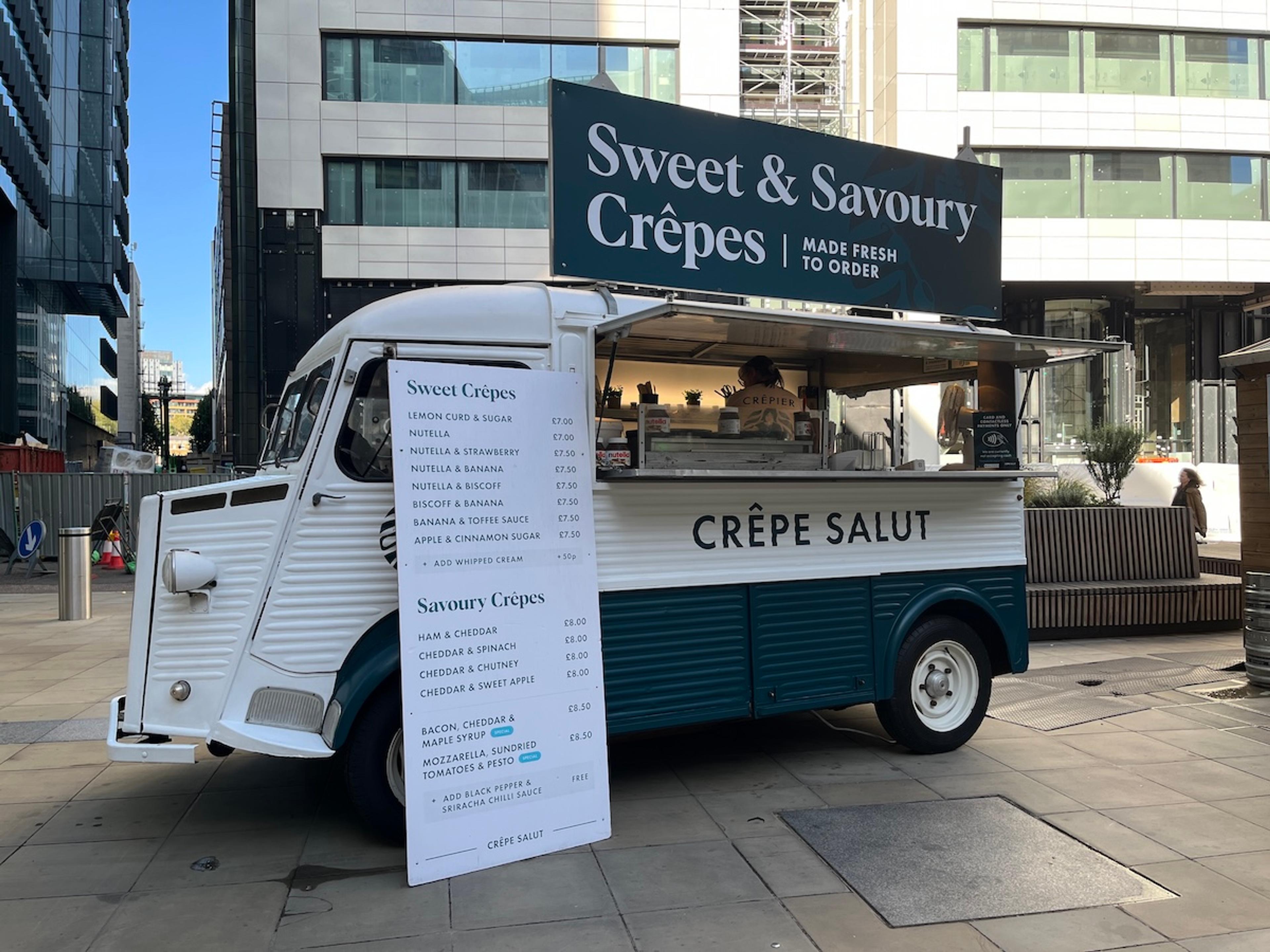 The crepe van in a city square with its menu board