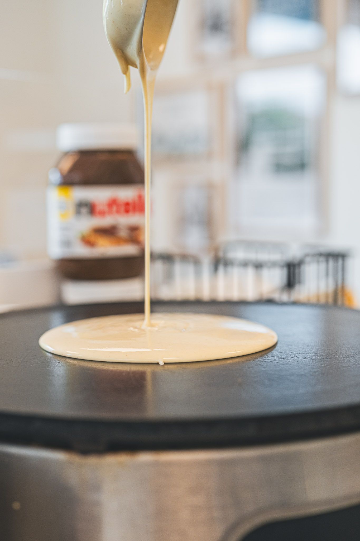 Nutella being drizzled onto a crepe on the griddle