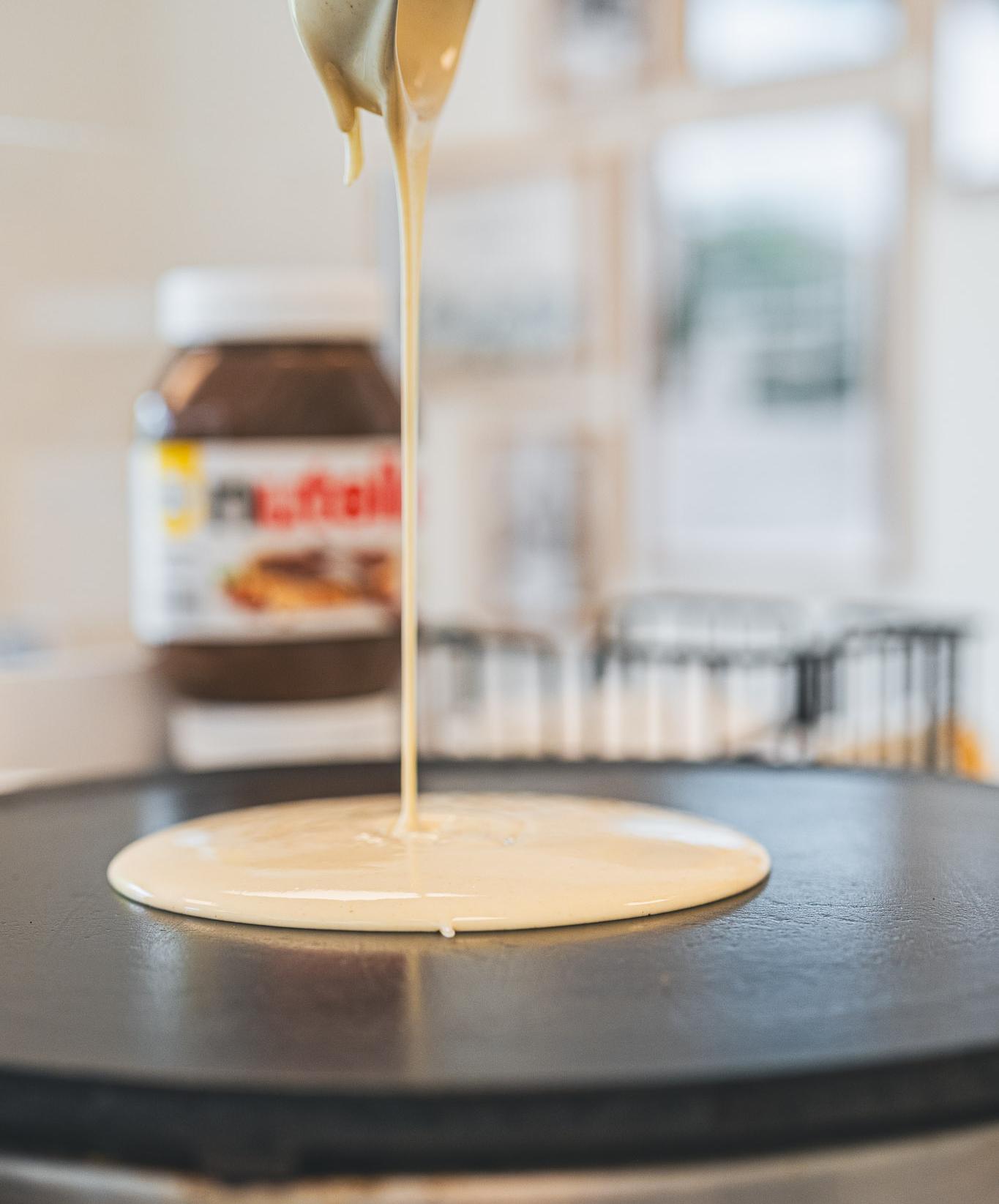 Nutella being drizzled onto a crepe on the griddle