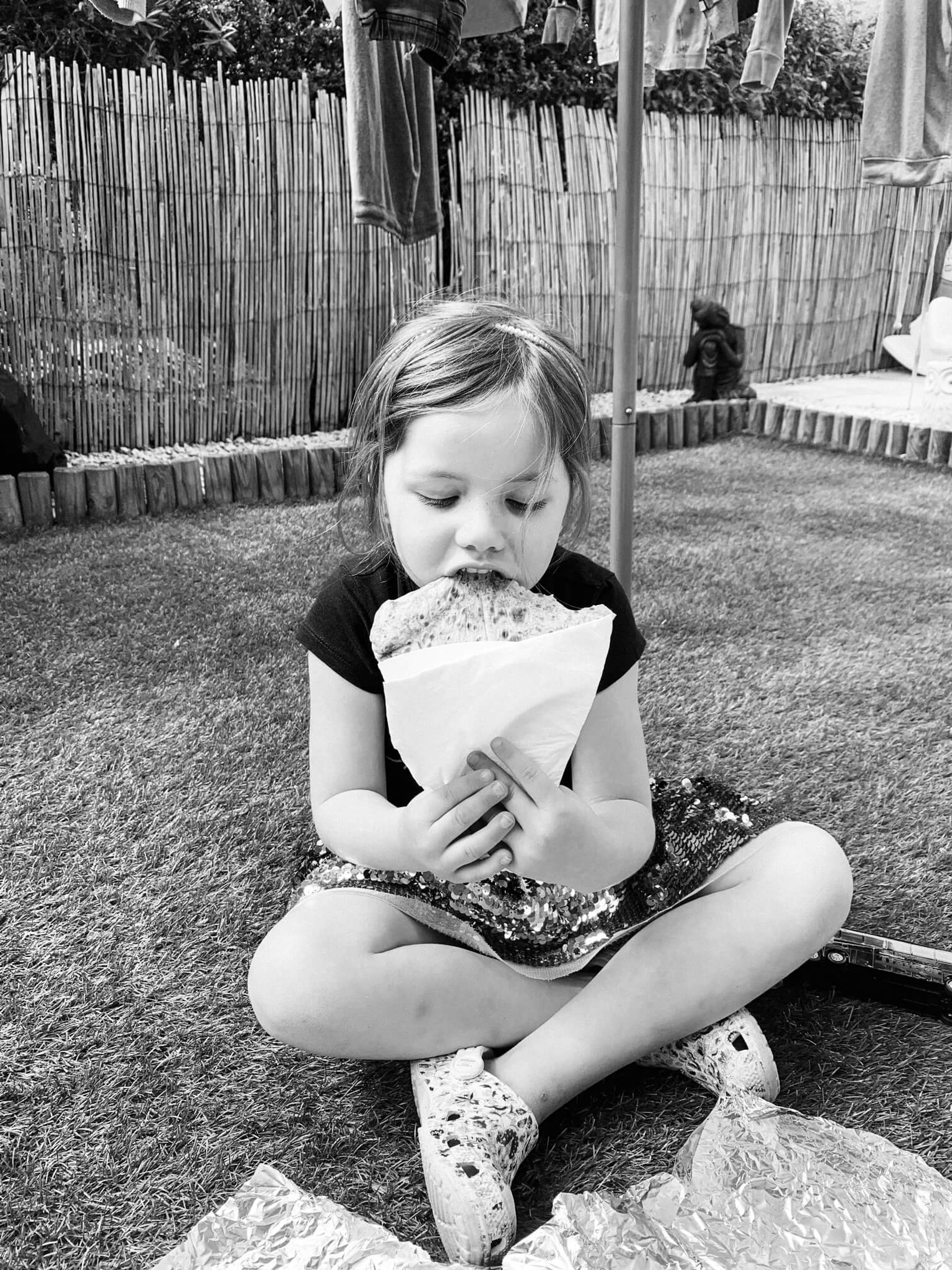 A child eating a crepe on the grass