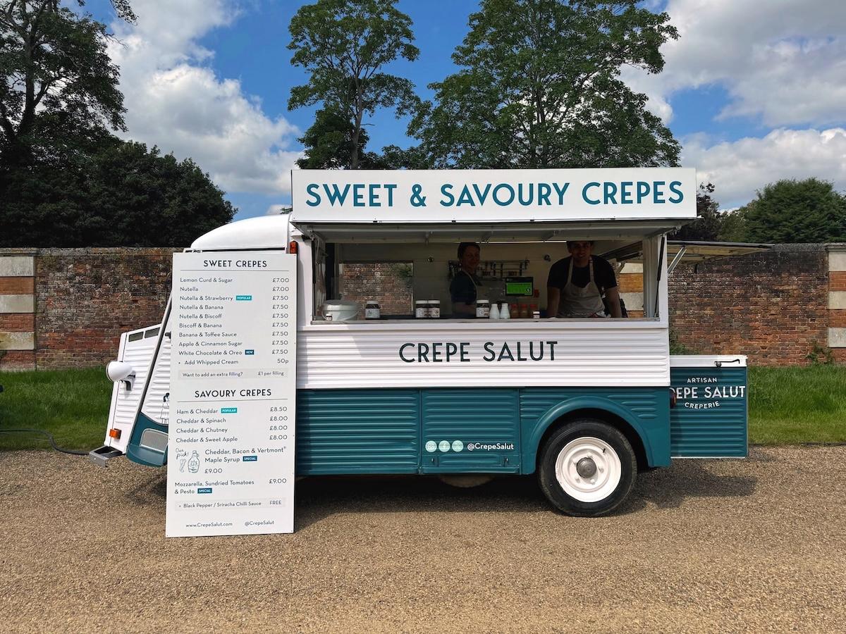 The crepe van with its menu boards set up by a garden wall