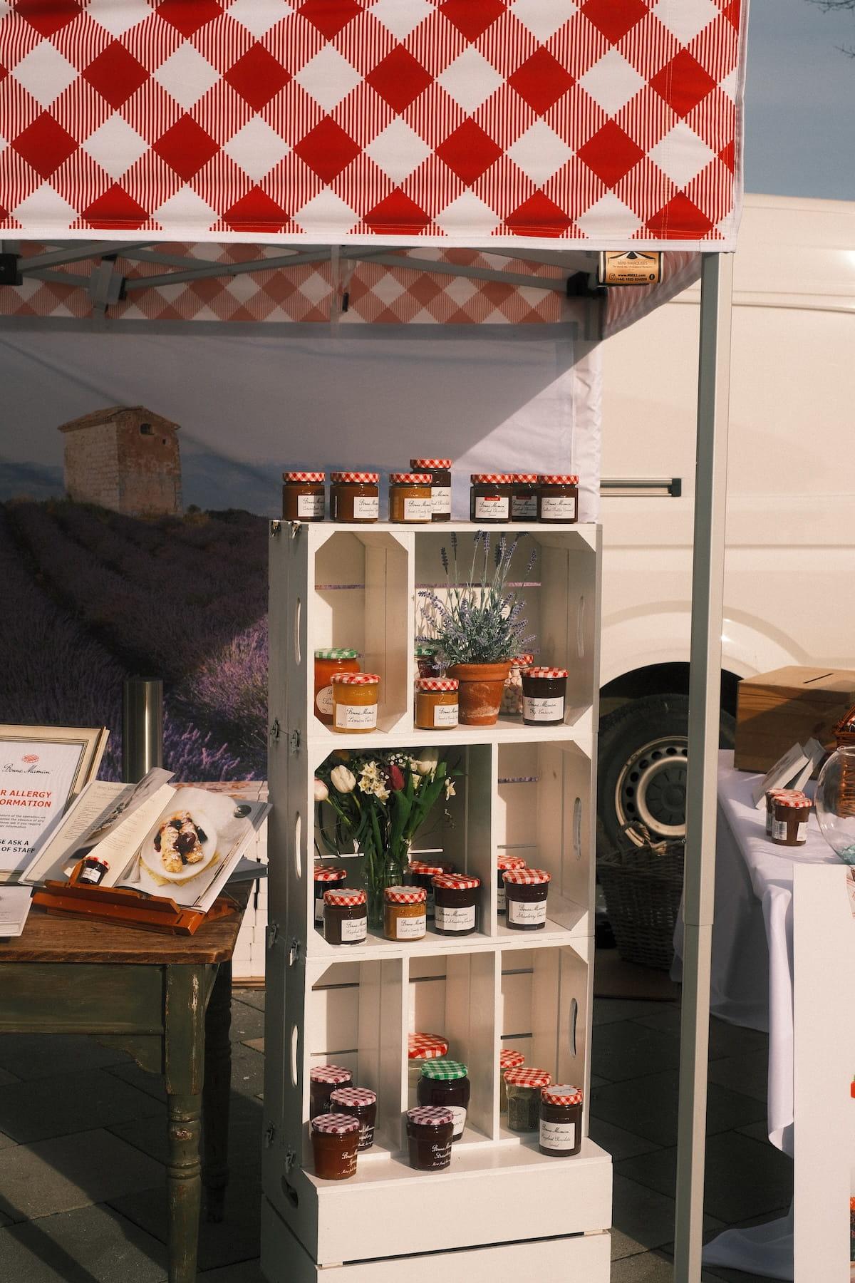 A Bonne Maman sampling stand with jars on crate shelves under a gingham awning