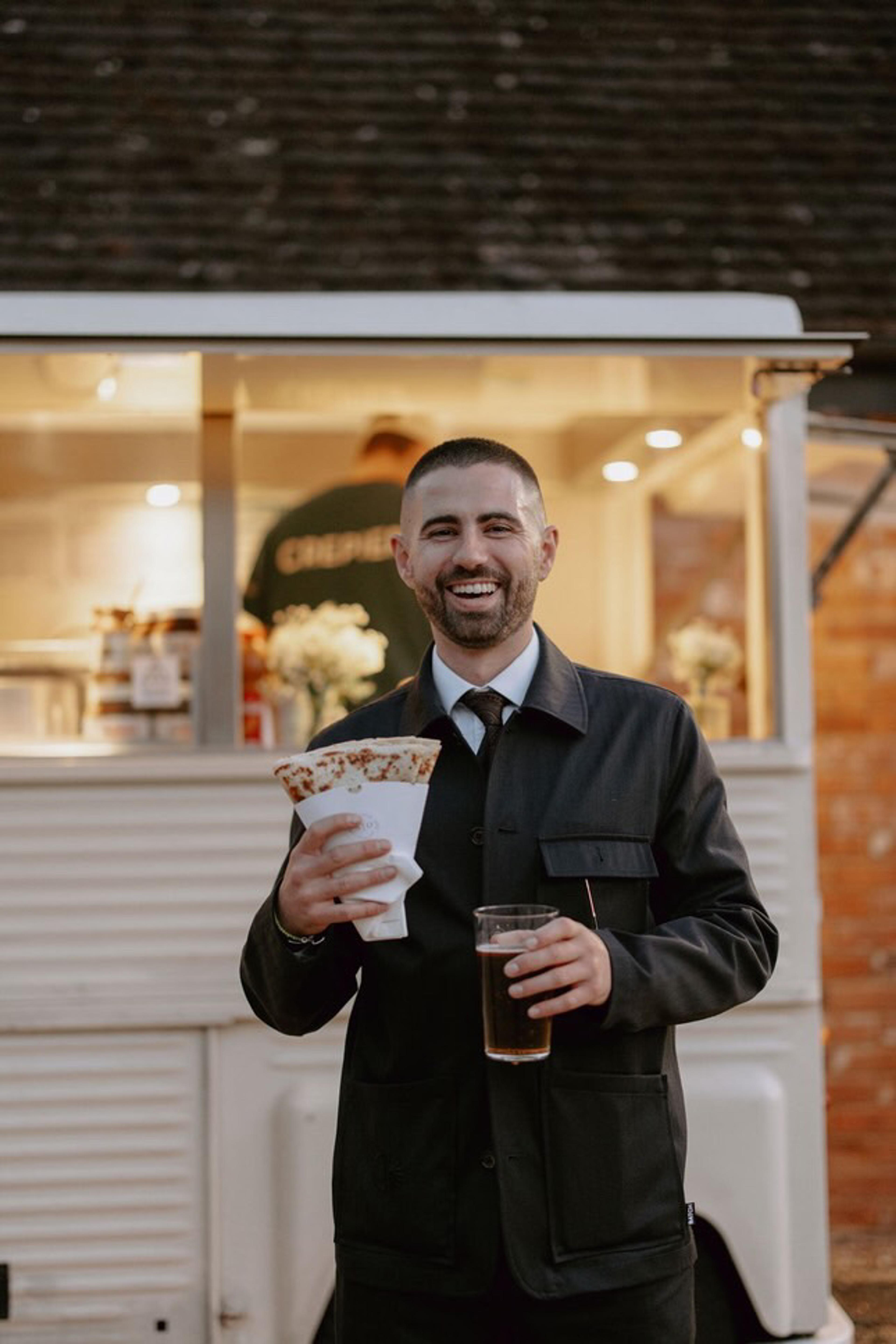 A guest holding a crepe and a pint beside the van
