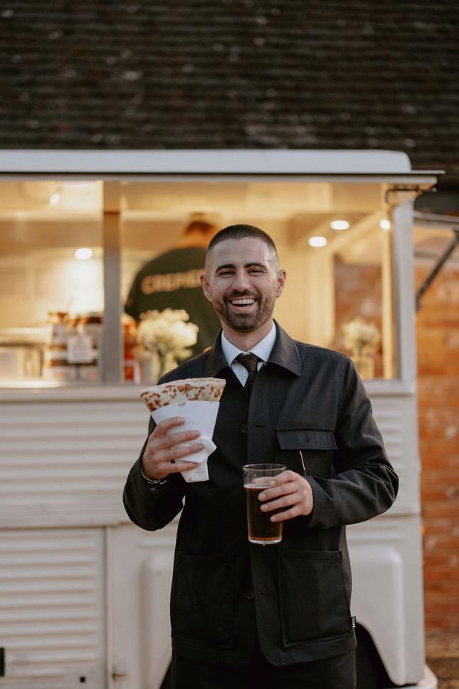 A guest holding a crepe and a pint beside the van