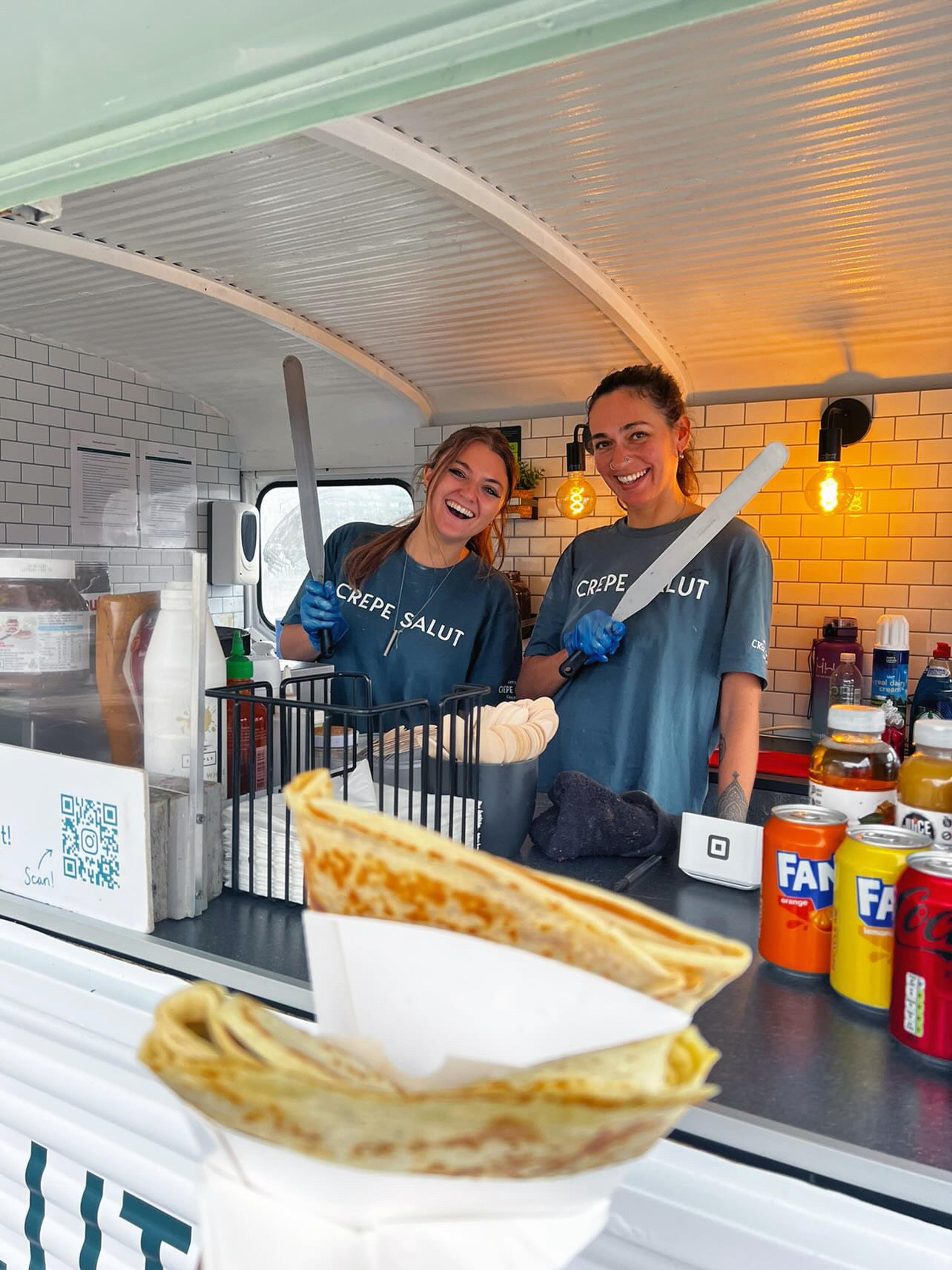 Two team members serving a crepe from the van hatch