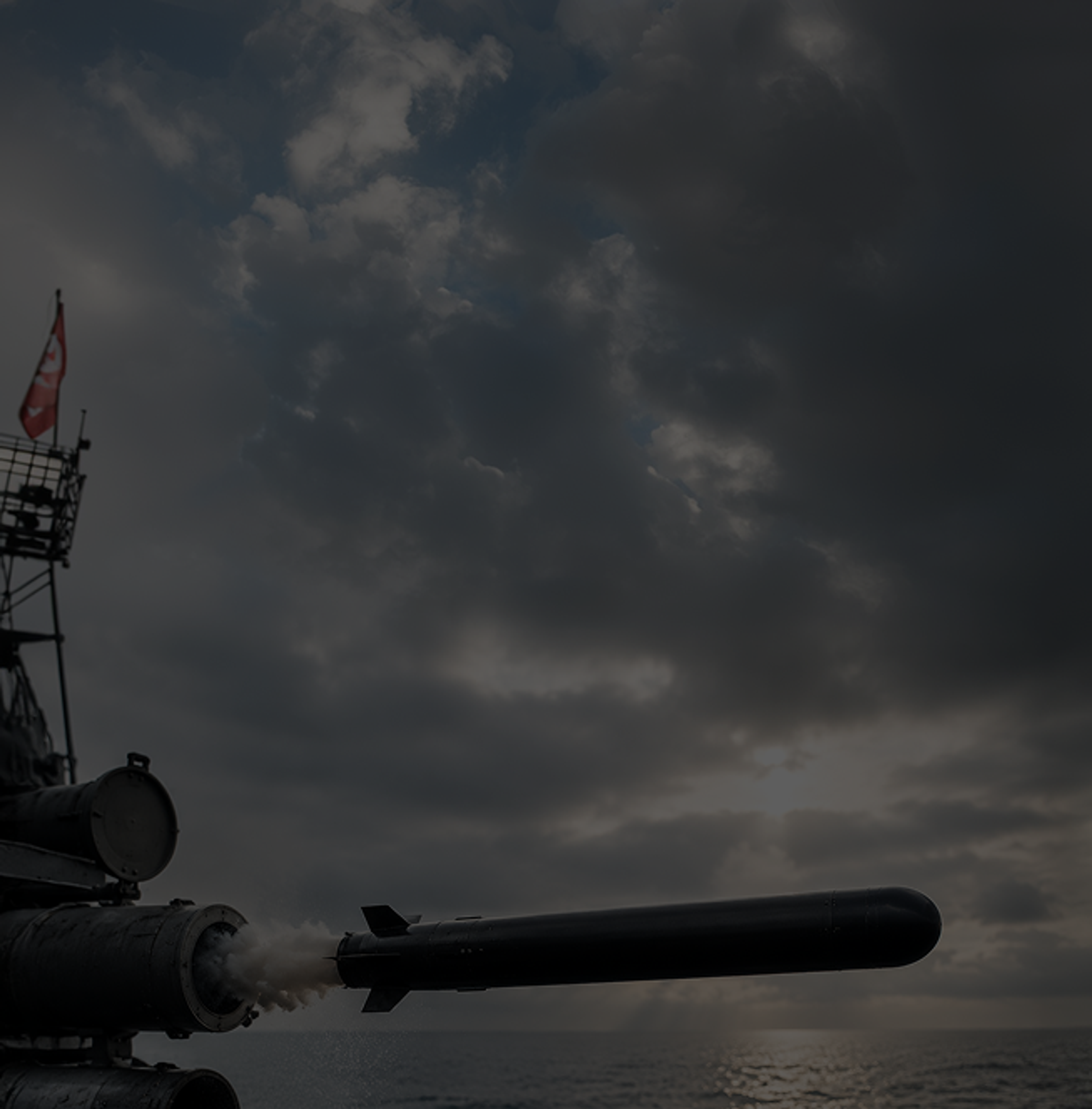A missile launching from the deck of a naval warship at sea under a heavy overcast sky