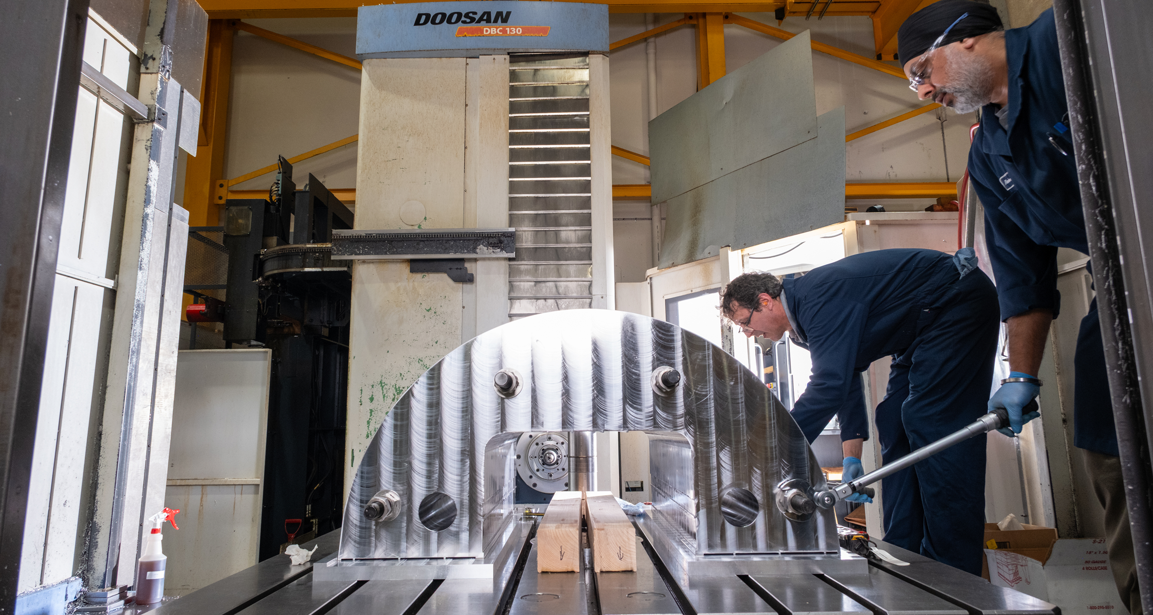 Two machinists setting up a large curved workpiece on a Doosan horizontal boring mill