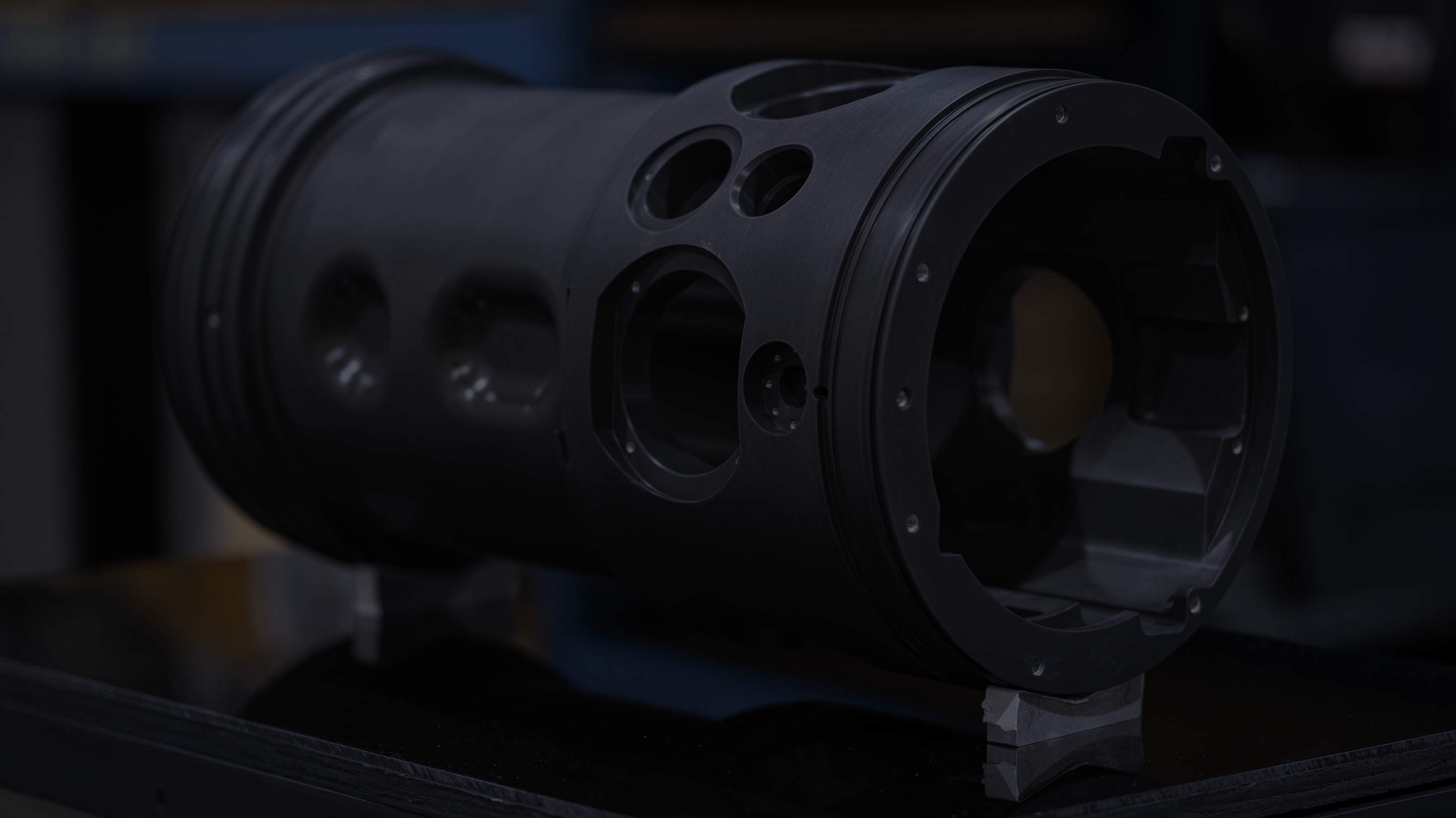 Close-up of a black anodised cylindrical housing with precision-bored optical apertures
