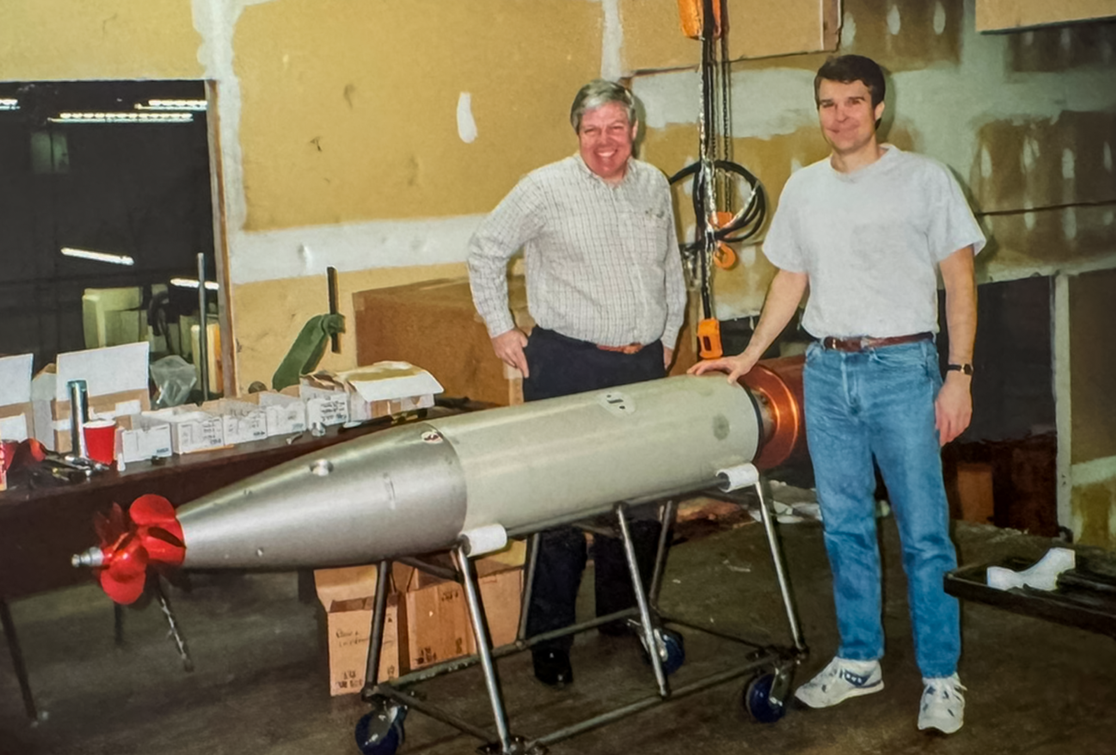 Two SICOM engineers standing beside an early training torpedo body in the workshop