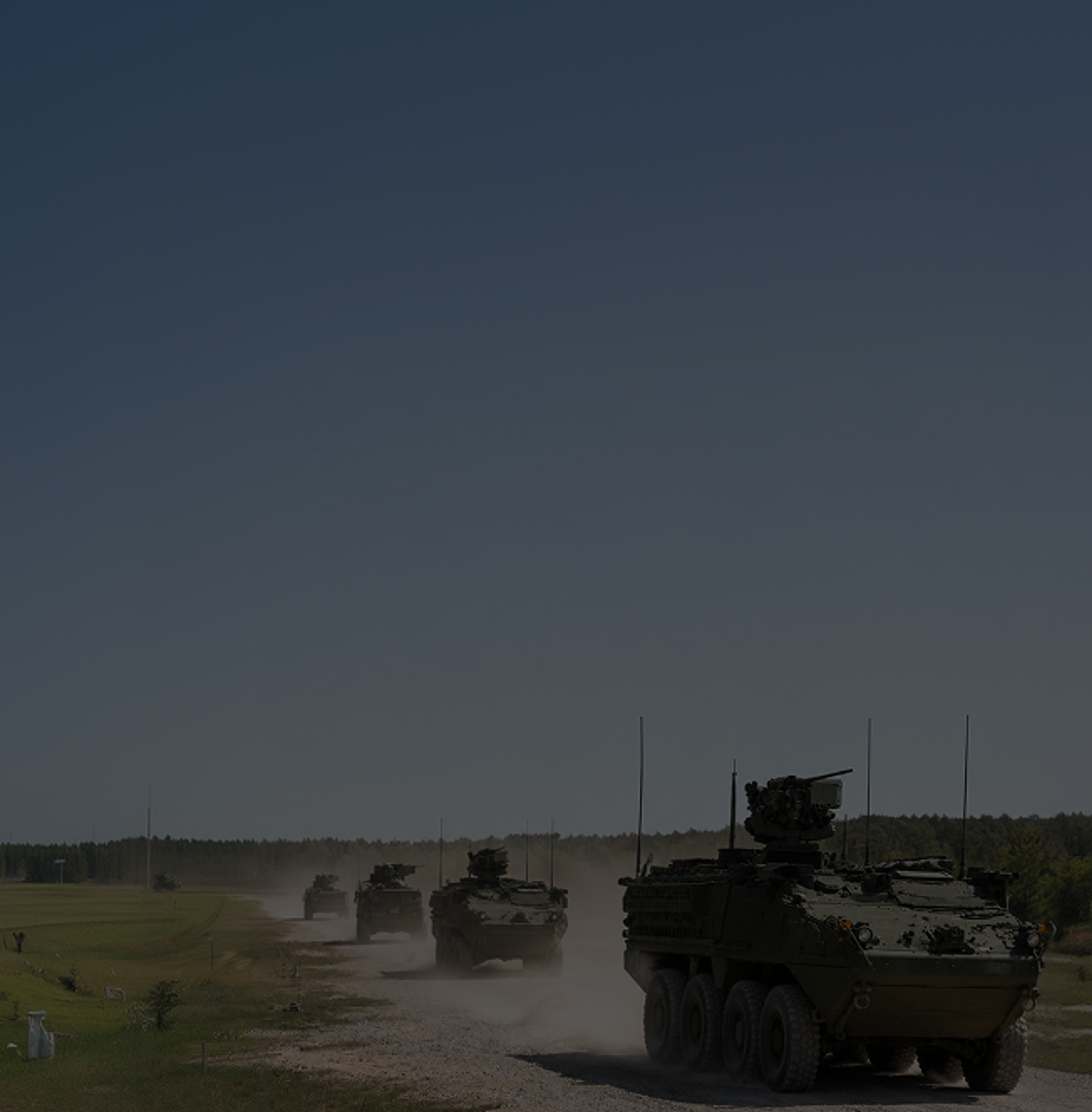 A convoy of eight-wheeled armored fighting vehicles advancing along a dirt road, raising a trail of dust