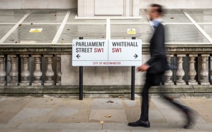 Personal walking past a road sign pointing to Parliament and Westminster