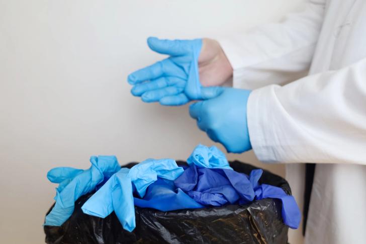 Single use surgical gloves being thrown in a bin after use