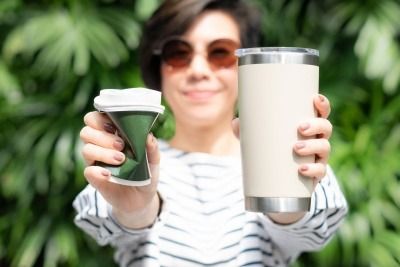 Woman holding up a reusable and disposable cup