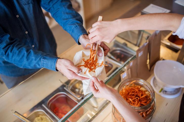 Hands of shop assistant serving customer in package-free store using reusable containers