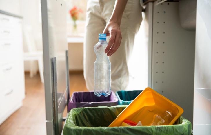 A person choosing which recycling bin to place a plastic bottle into