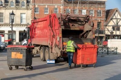 Bin operative loading an 1100 litre bin onto back of a refuse collection vehicle in Swindon