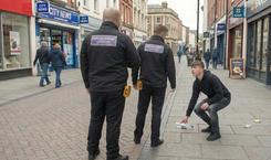 Litter enforcement officers instruct young man to pick up litter in a town centre