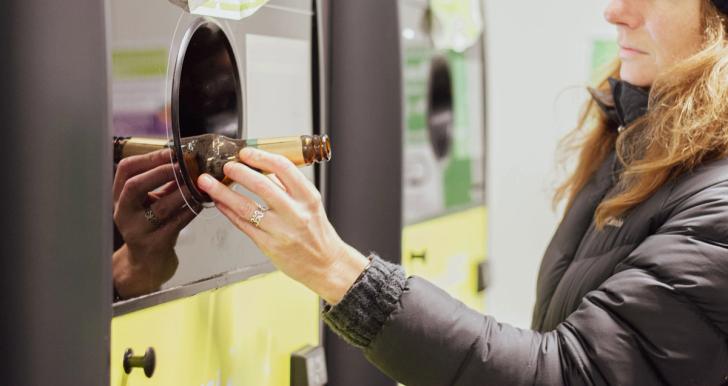 Woman placing a glass bottle in a deposit return scheme reverse vending machine