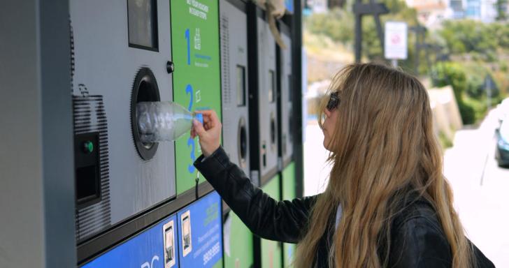 Female student putting a plastic bottle into a deposit return machine