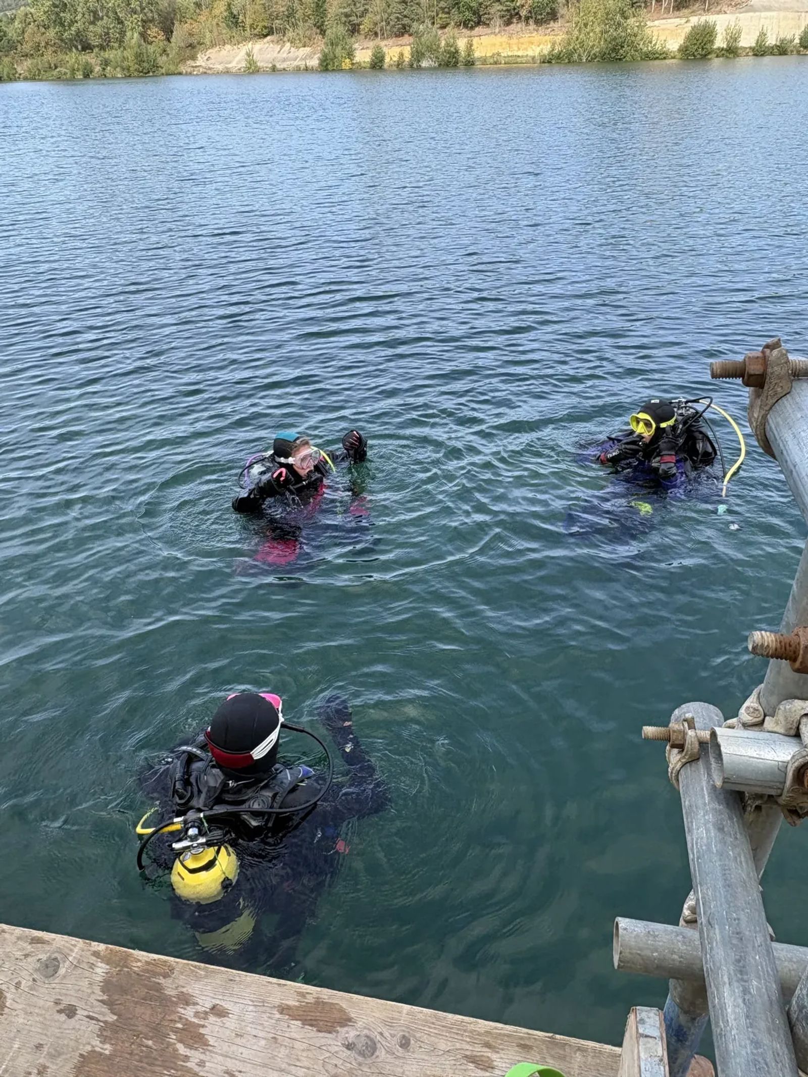 Three divers on the surface of the quarry next to the jetty, ready to descend