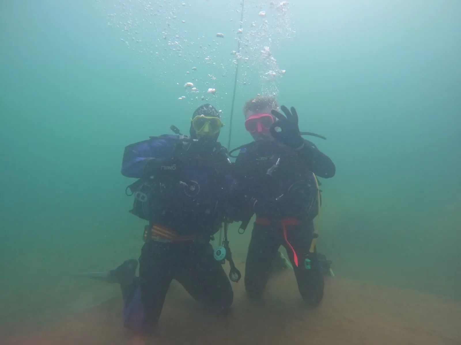 Two divers kneeling on the bottom of the quarry giving the OK signal, the shot line running up behind them