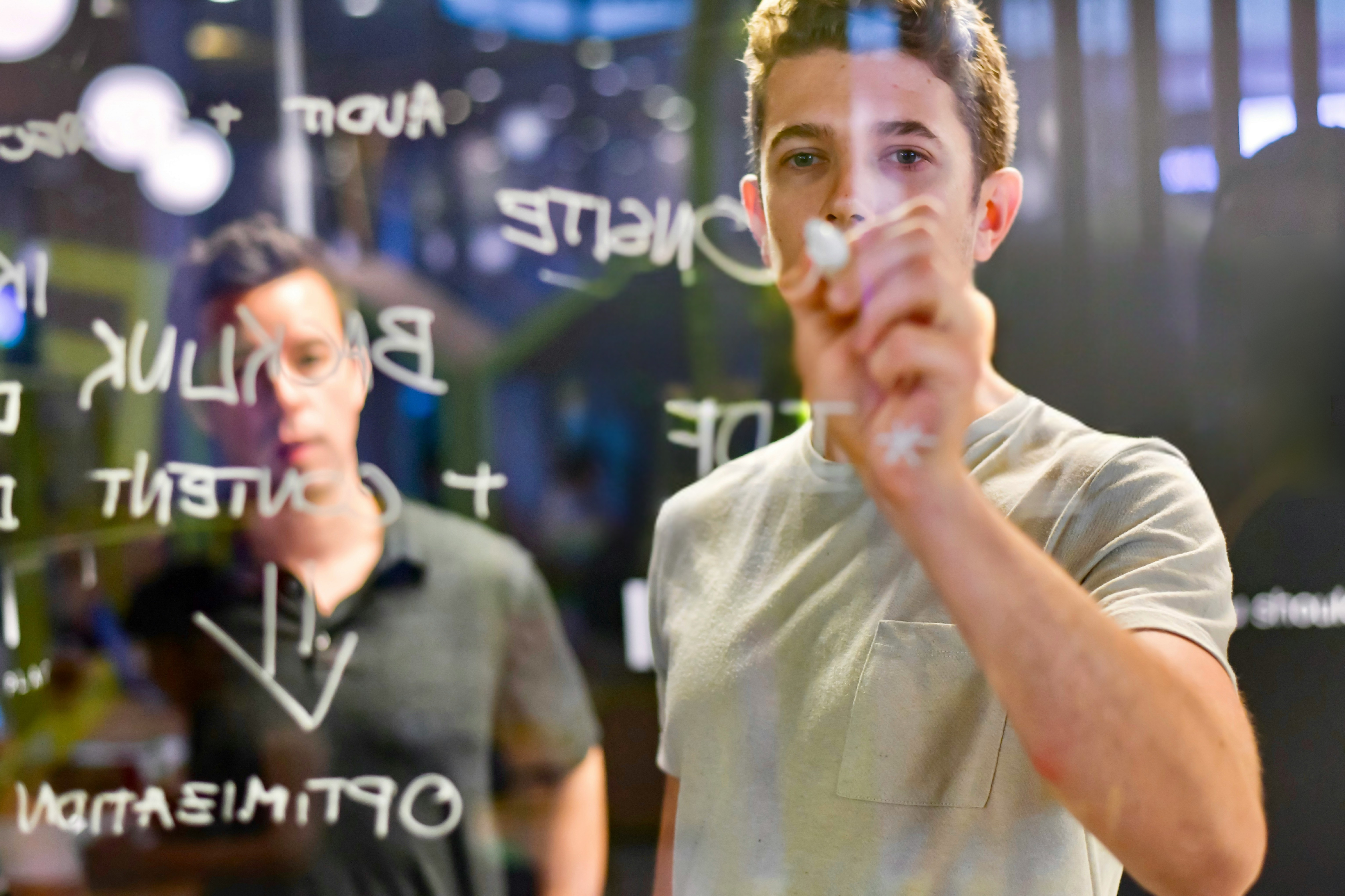 two persons writing on a glass board