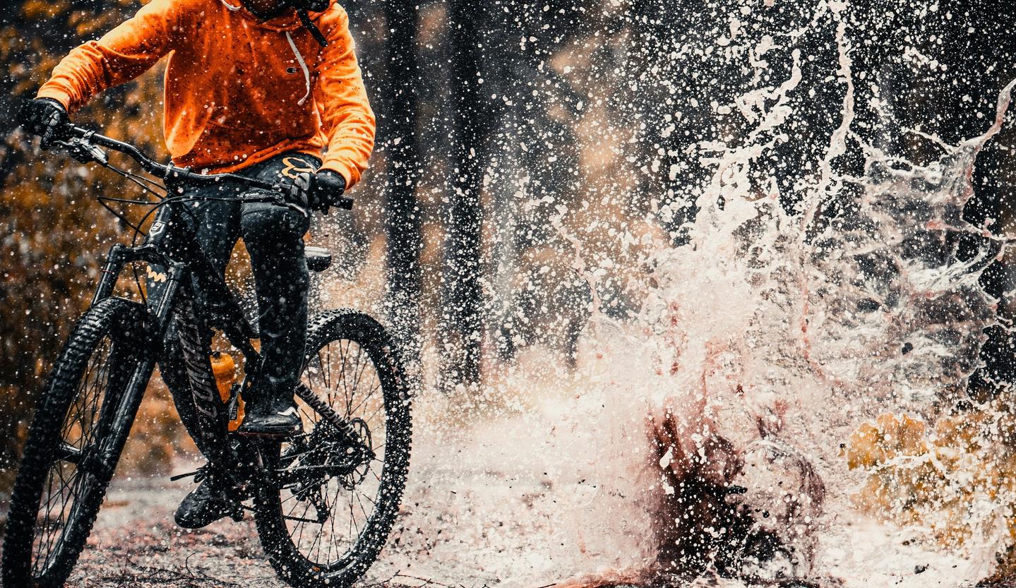 mountain biker creating huge splash by riding through a puddle in a wooded forest