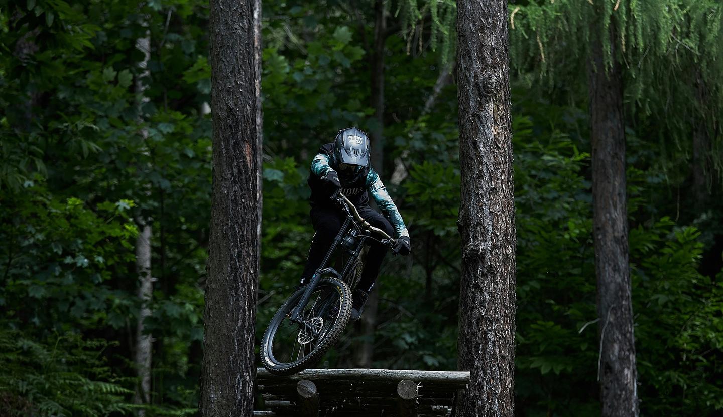 mountain biker jumping off large ramp between two pines