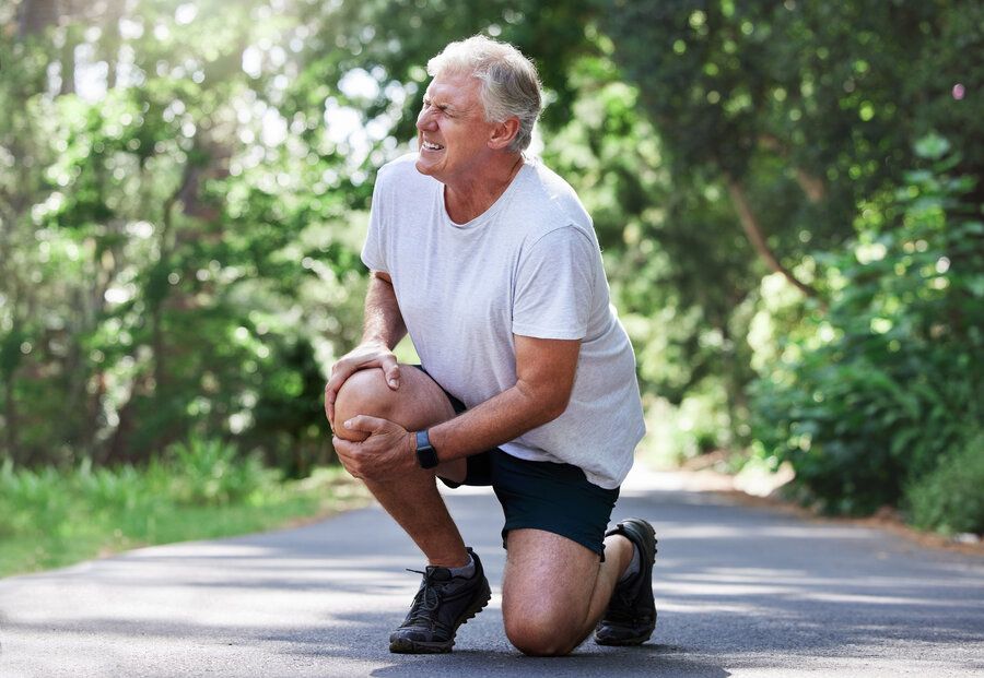 Man outside exercising grimaces in pain and holds his knee due to ACL tear