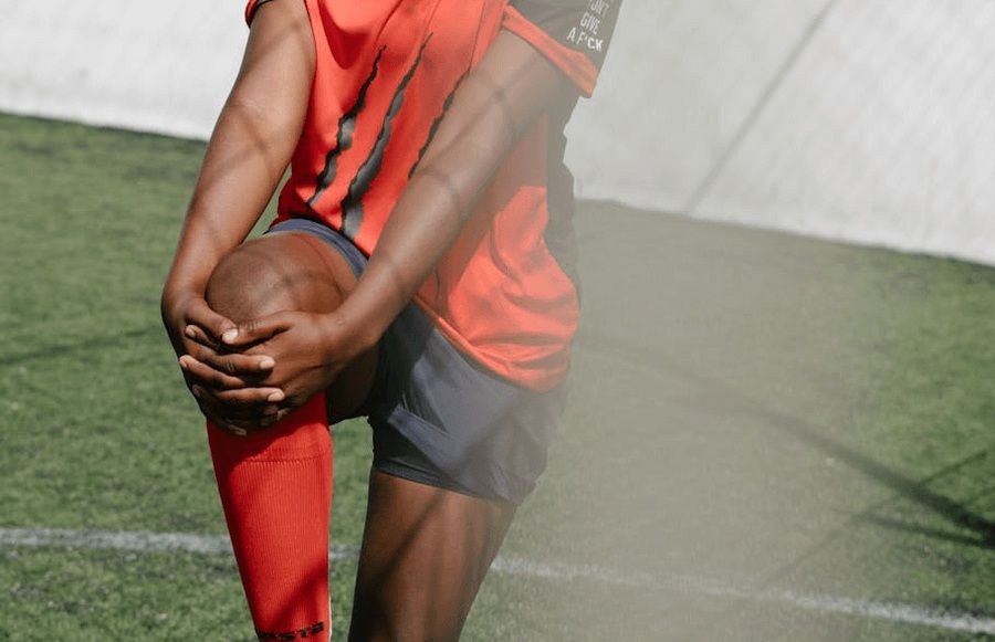 Closeup of a soccer player holding his knee with two hands, stretching, has reclaimed knee mobility after knee surgery in San Francisco