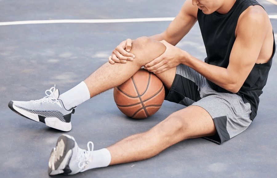 Basketball player sitting on court holding his knee from a nagging injury, seeking care from the best orthopedic surgeon in San Francisco.