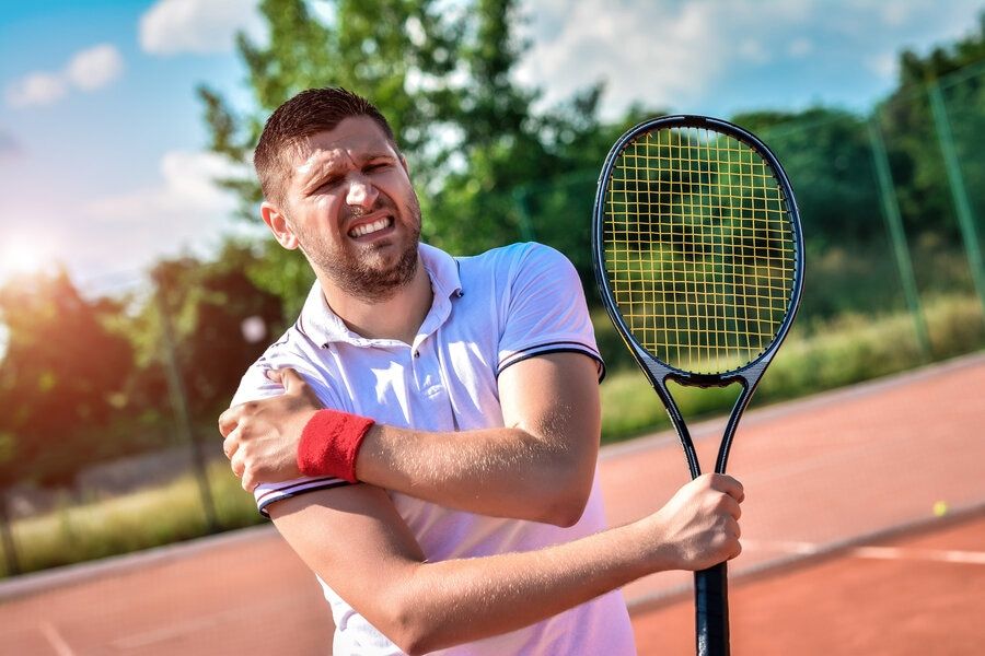 Man playing tennis grimaces in pain due to shoulder overuse injury