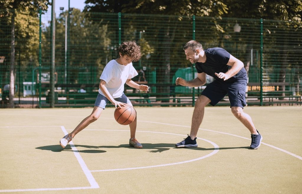 Active father teaching his son to play basketball on an outdoor court, representing recovery with orthobiologics for faster healing guided by the best orthopedic surgeon in San Francisco, CA