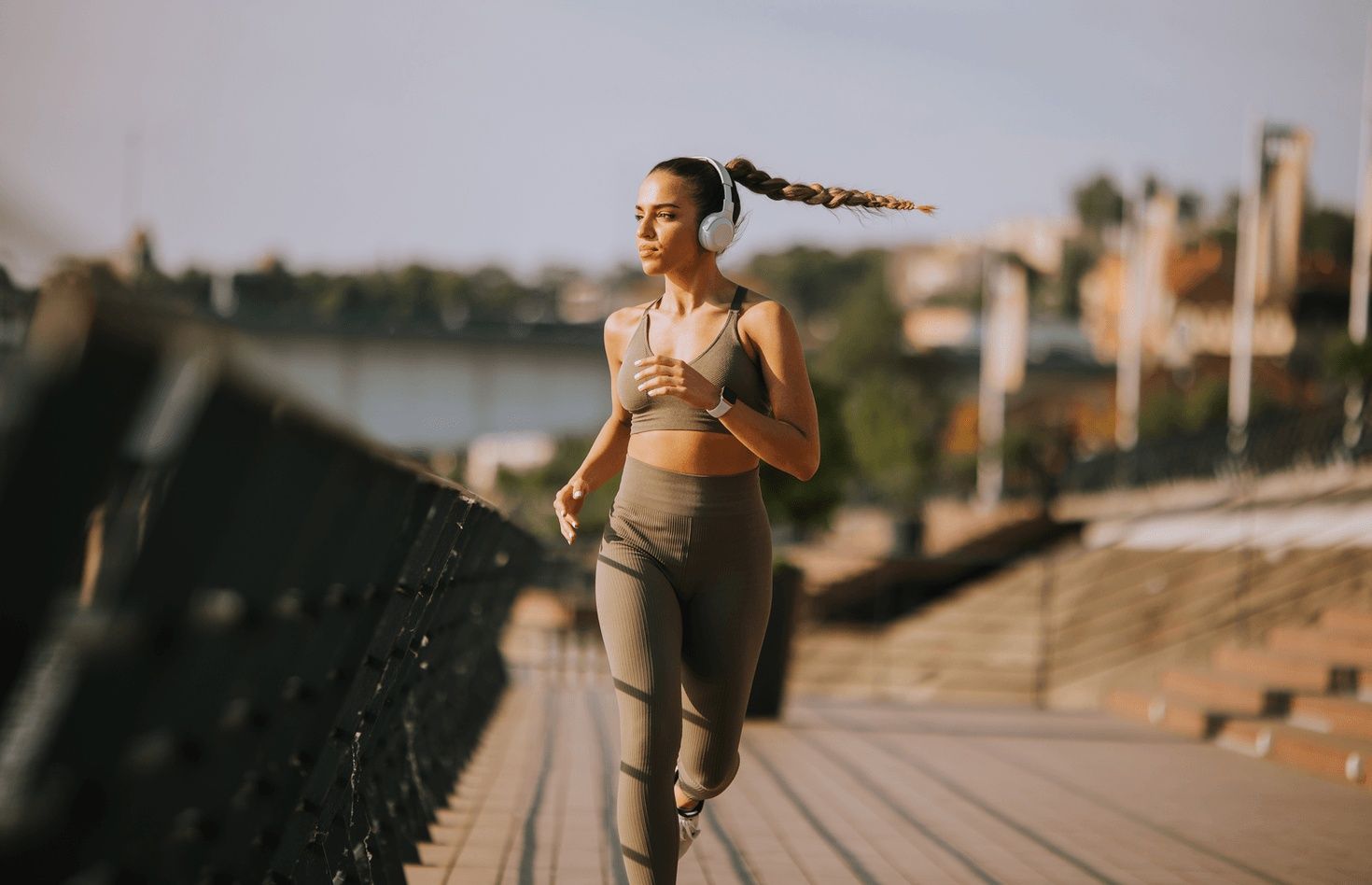 Woman athlete jogging outdoors on a waterfront path while wearing wireless headphones and athletic wear, representing active recovery, joint repair for weekend warrior athletes, and care from the best orthopedic doctor in San Francisco, CA.