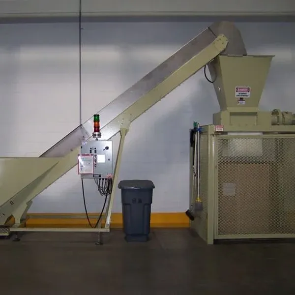 A large industrial shredder with a conveyor attachment in a warehouse