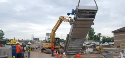 SCREENMASTER CS mechanical bar screen being lifted above a concrete wastewater channel by a crane