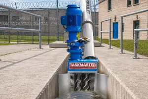 TASKMASTER grinder with SPIRALIFT screw conveyor installed in a concrete wastewater channel outside a correctional facility with razor-wire fencing